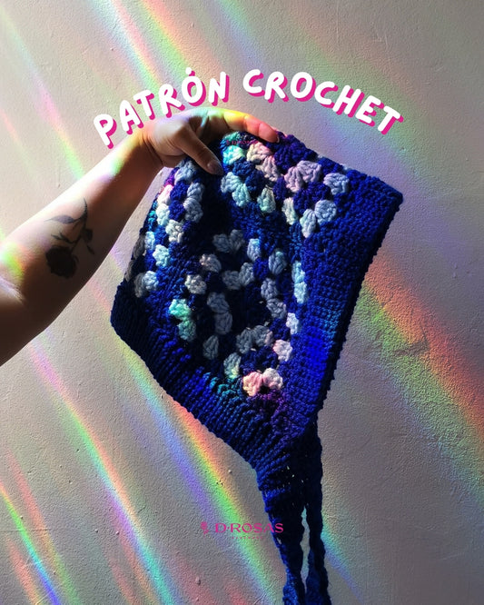 Gorro tipo bonnet hecho de cuadros de granny square, se hace bufanda el cuello con tiras largas, está siendo sostenida por una mano que muestra el brazo con el tatuaje de una rosa. Las palabras patron crochet en la parte superior de la imagen.